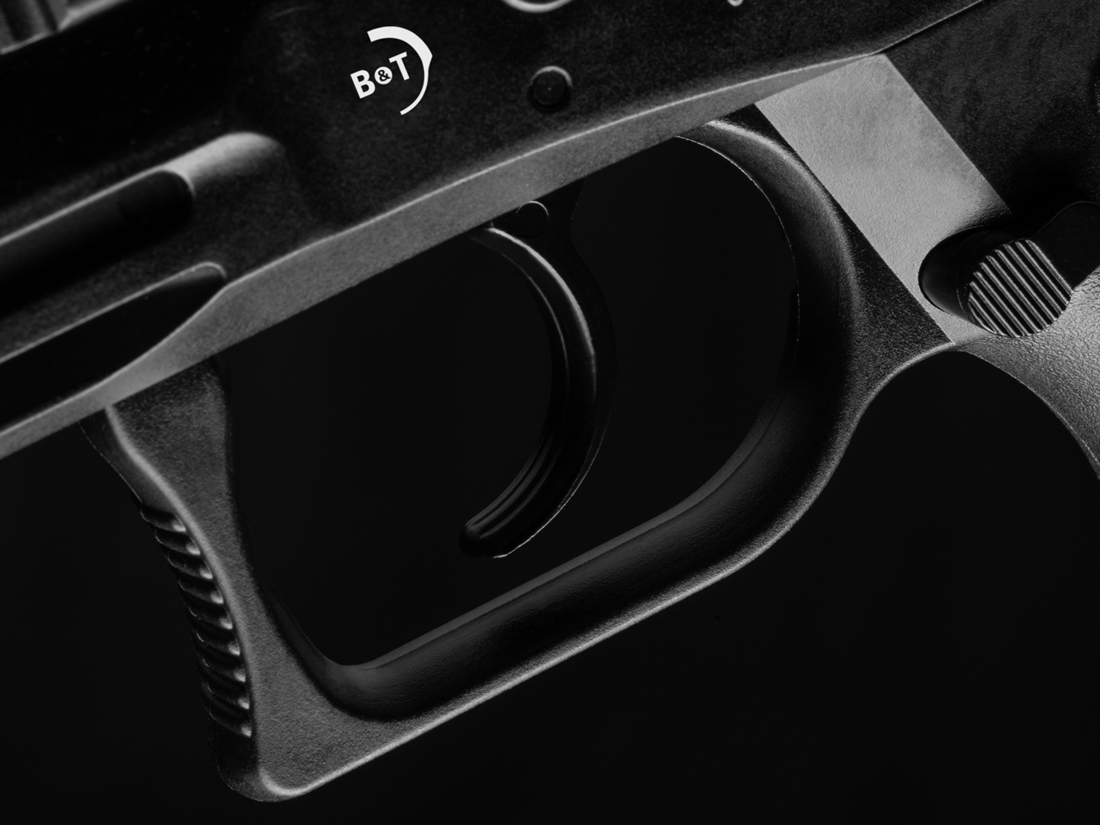 ASG B&T USW A1 black GBB CO² - ab 18 Jahren Nahaufnahme eines schwarzen Abzugs mit "B&T" Logo, Detail einer Airsoft-Waffe.